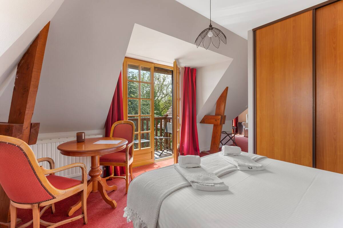 A bedroom with a bed, a wooden chair, a small table, and a window with curtains.