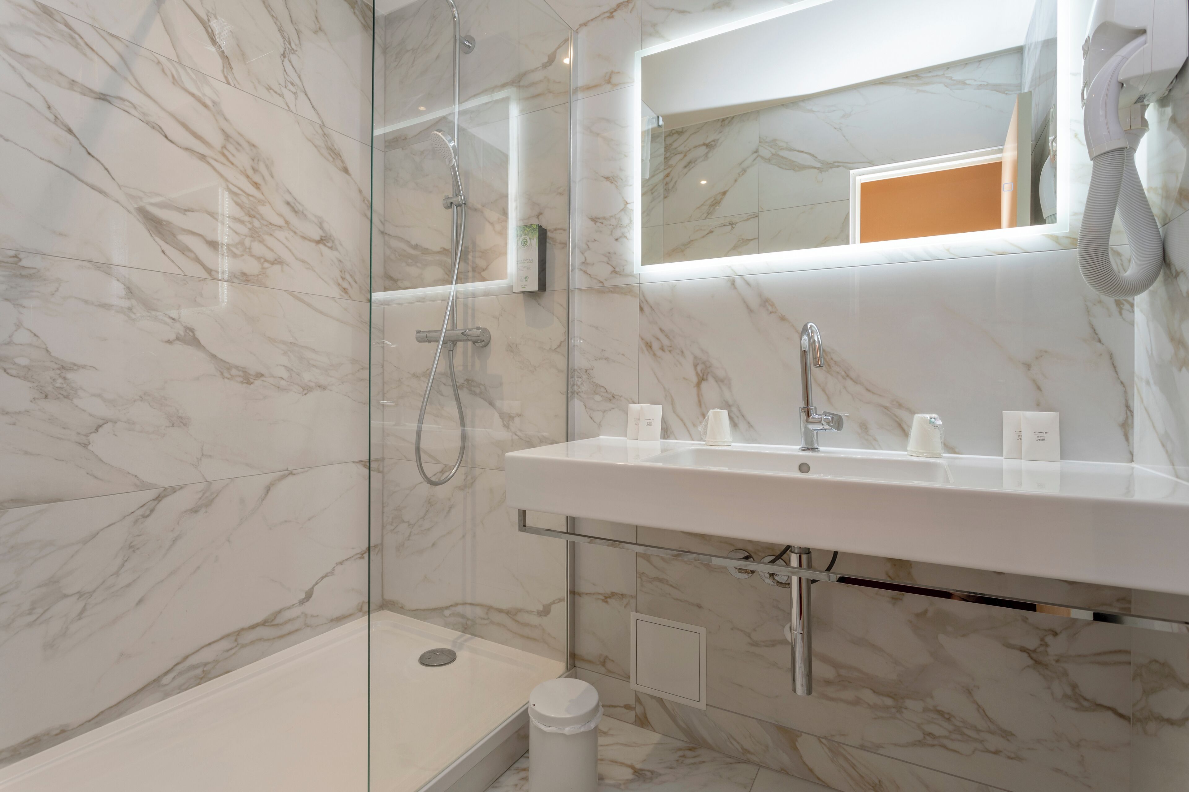 Un baño moderno con ducha de mármol, cabina de ducha con mampara de vidrio, un espejo grande y un secador de pelo incorporado.