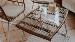 Un café acogedor con mobiliario de mimbre, una mesa de vidrio con una botella y la carta, y grandes ventanales con vista a la calle.