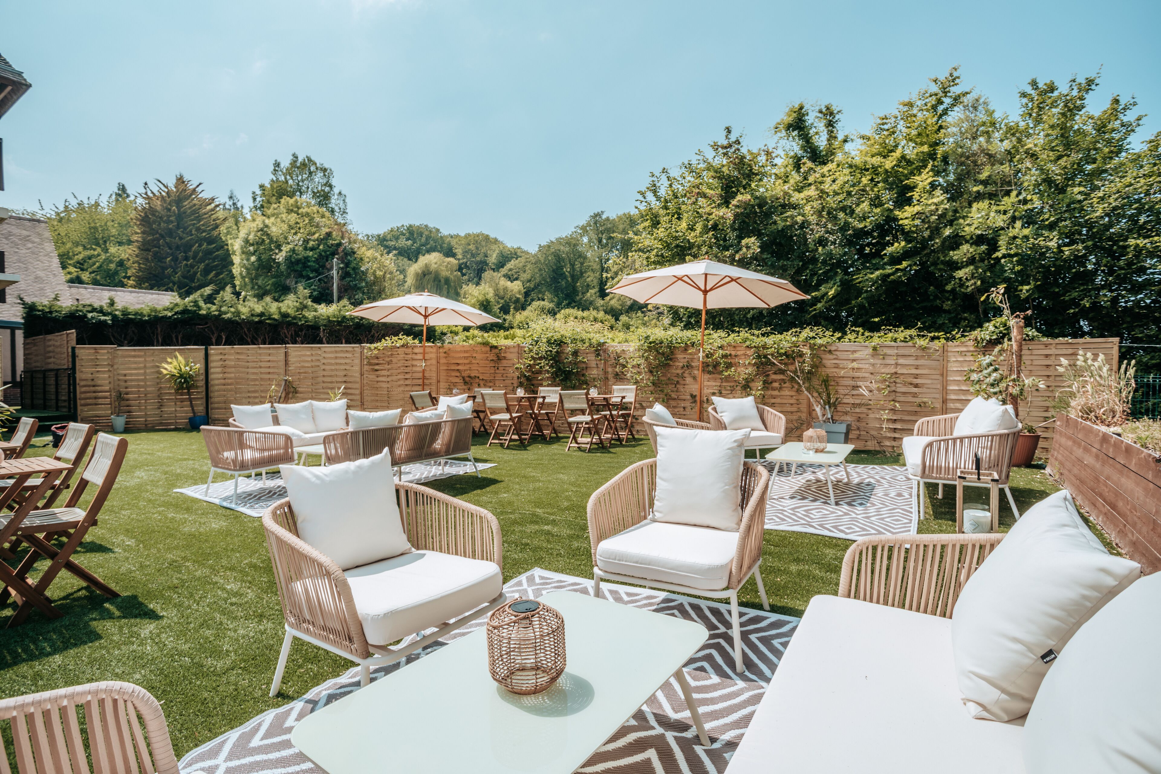An outdoor patio area with wicker furniture, white cushions, and two umbrellas.