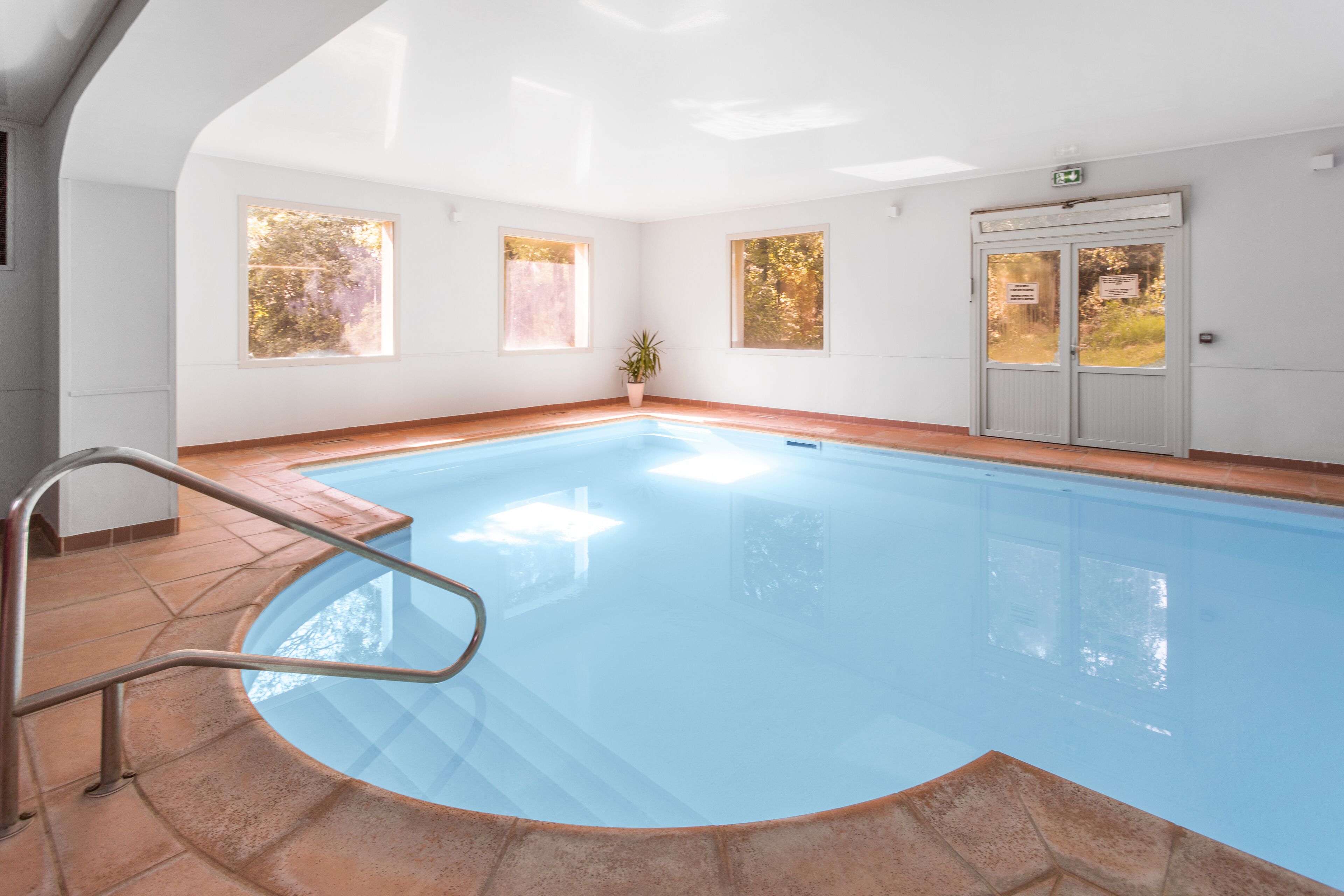 An indoor swimming pool with clear blue water, surrounded by white walls and large windows.