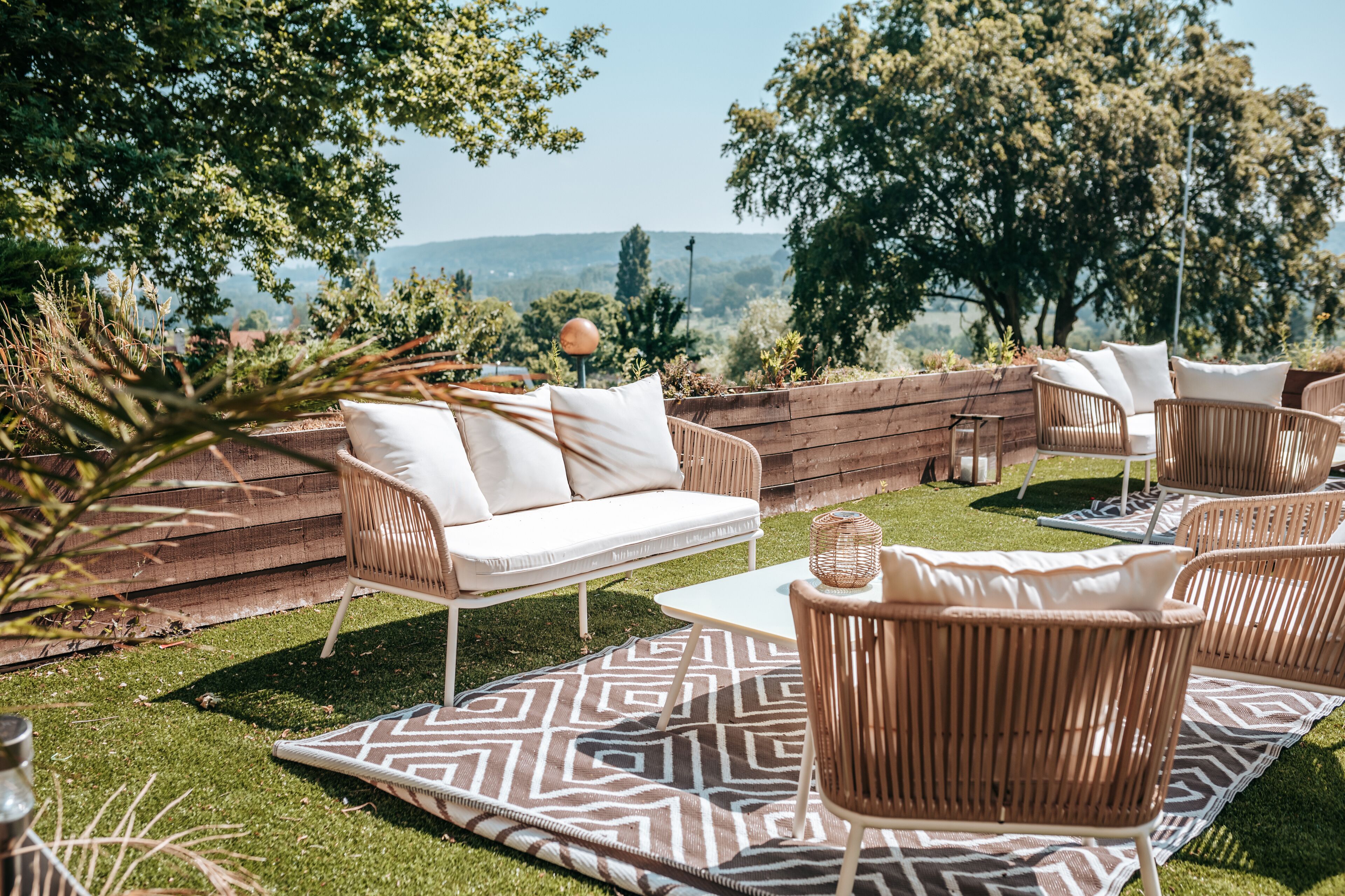 An outdoor seating area with wicker furniture, a patterned rug, and a view of the landscape.