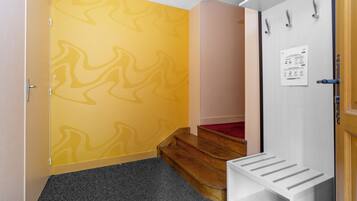 A hallway with a patterned yellow wall, a wooden staircase, and a white door with a notice.