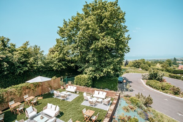 Un patio exterior con mobiliario y una piscina, rodeado de follaje y vistas a la carretera.