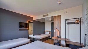 A modern hotel room with three single beds, a small desk, a mirror, and a coat rack. - B&B HOTEL Paris Créteil (Creteil)