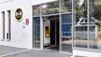 L’entrée d’un hôtel-restaurant avec une porte en verre, un distributeur automatique jaune et une enseigne.