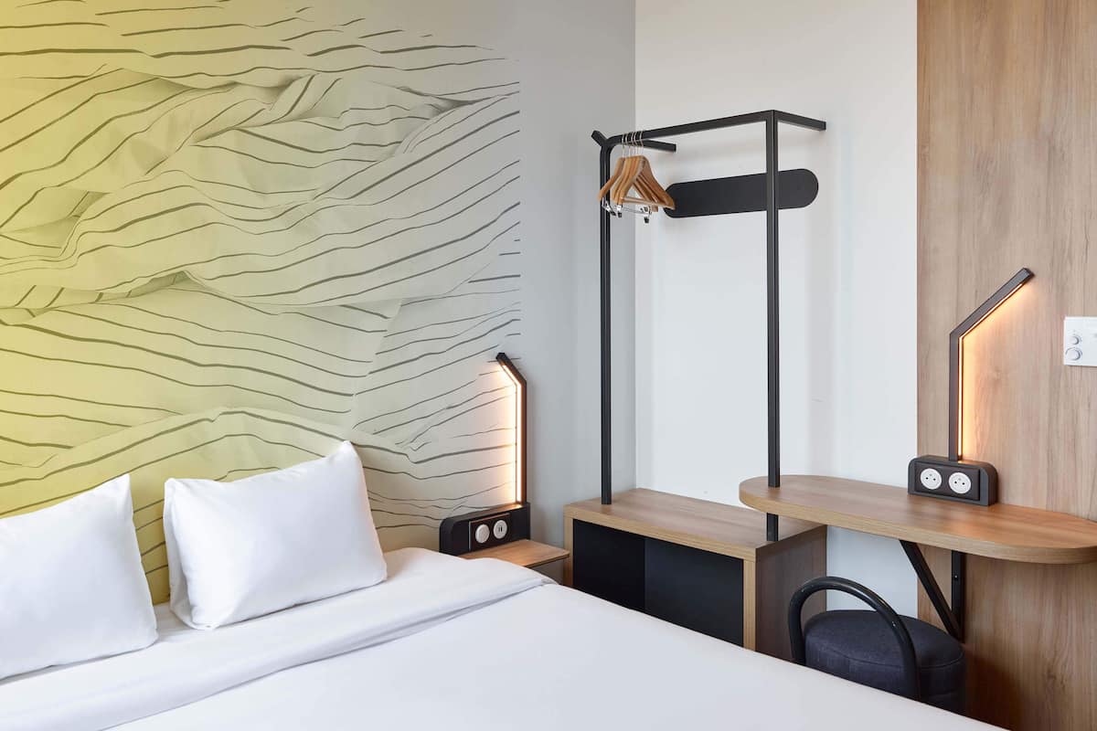 A hotel room with a bed, bedside tables, a desk, a hanging light, and a wall with a textured pattern.