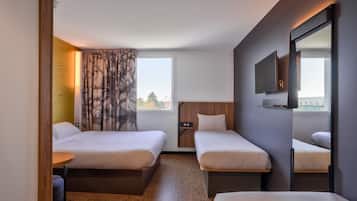 A hotel room with two single beds, a small table, a TV, and a window with curtains.