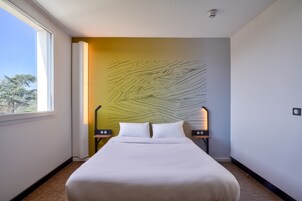 Una habitación de hotel moderna con una cama grande, una obra de arte original en la pared y vistas a árboles por la ventana.