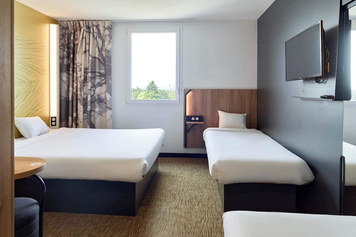 A hotel room with two beds, a TV, a window, and a view of the outdoors.