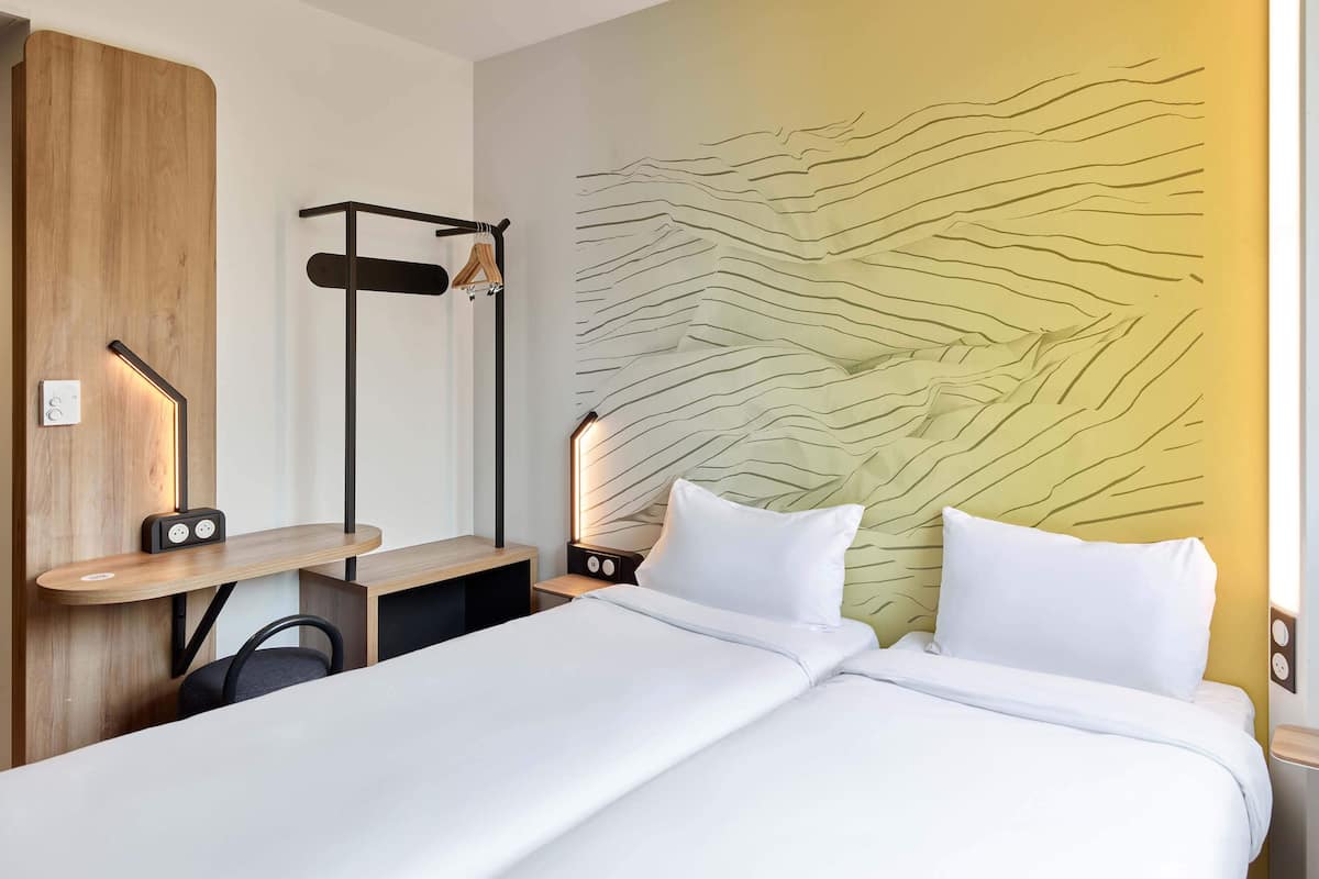A hotel room with a bed, bedside tables, a wall-mounted shelf, and a headboard with a unique design.