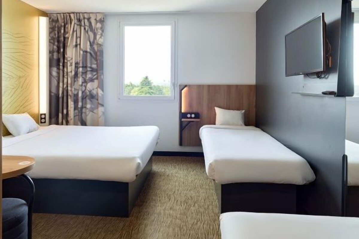 Une chambre d’hôtel avec deux lits, une télévision, une fenêtre et une vue sur la verdure environnante.