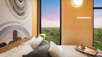 A bedroom with a bed, pillows, a tray with a croissant, and a view of a green landscape through a window.