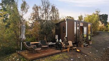 Uma cabana pequena com varanda, área de estar ao ar livre e lareira.