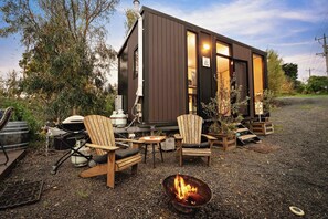 Une petite cabane avec un foyer, des sièges d’extérieur et un barbecue.