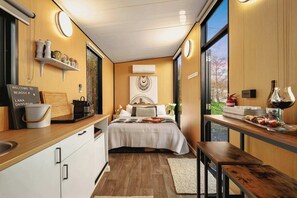 Habitación de hotel compacta con cama, kitchenette y vistas a través de un ventanal grande.