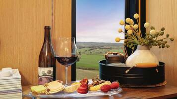 A table with a wine bottle, glass, cheese, fruits, and a vase with flowers.
