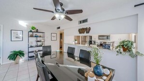 Una cocina moderna con electrodomésticos de acero inoxidable, un comedor con mesa y sillas de vidrio, y un ventilador de techo.