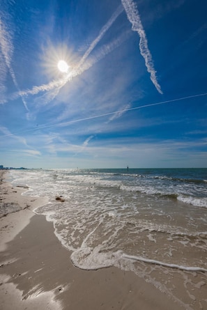 A beach with waves, a clear sky, and contrails.