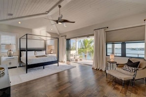 Ein Schlafzimmer mit Himmelbett, einem Balkon mit Vorhängen, einem Sessel und Blick auf das Wasser.