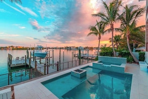 Un espace piscine au bord de l’eau, avec un quai, des palmiers et une vue imprenable sur le coucher de soleil.