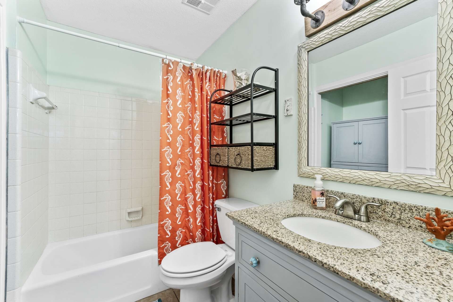 Un baño con una bañera blanca, un inodoro, un lavabo con encimera de granito y un espejo con marco decorativo.