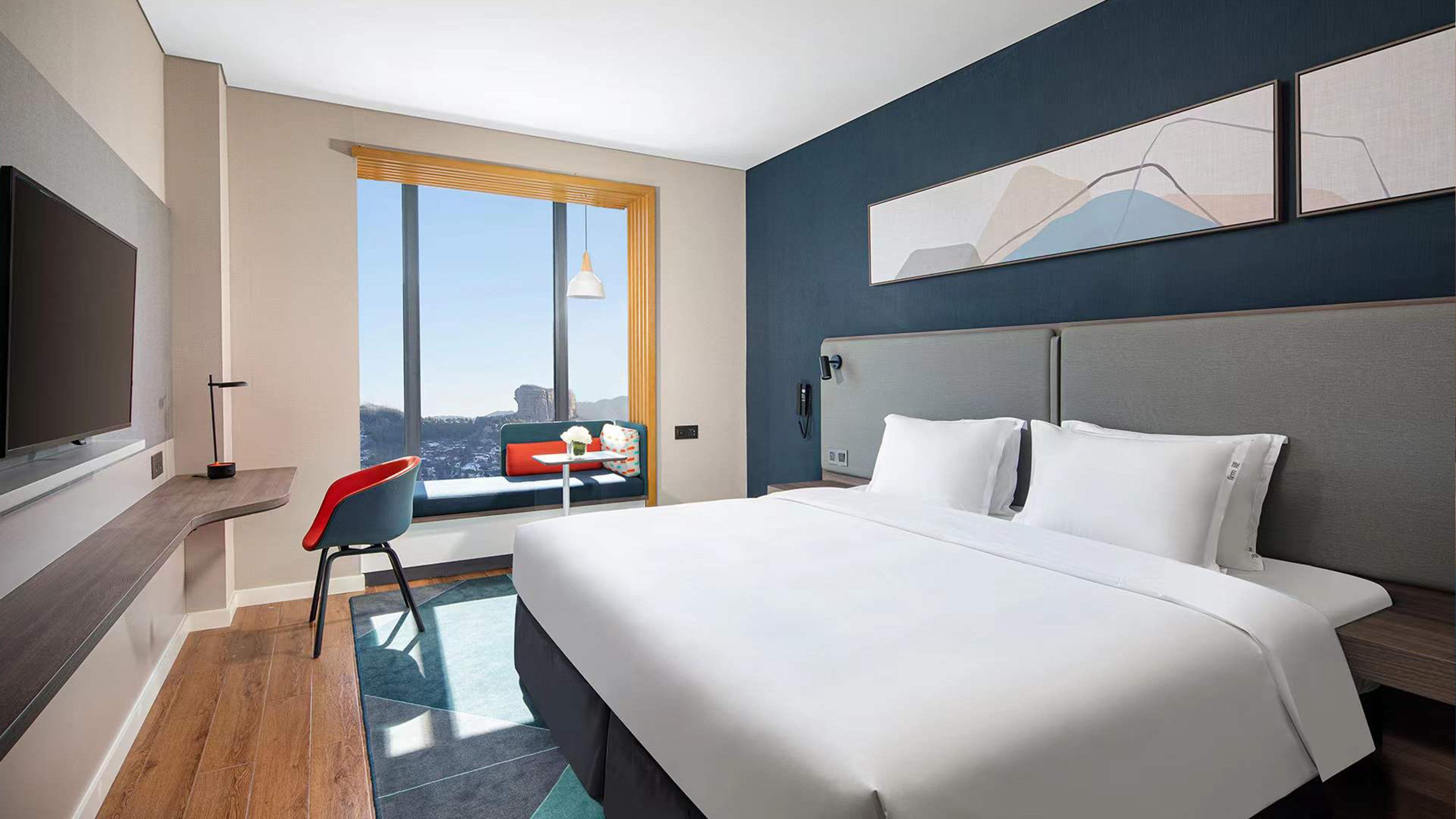 A modern hotel room with a large bed, a seating area with a view, and a flat-screen TV.