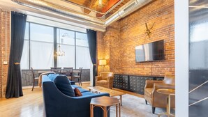 A modern living room with a brick wall, leather sofas, a flat-screen TV, and a dining area with a wooden table and chairs.