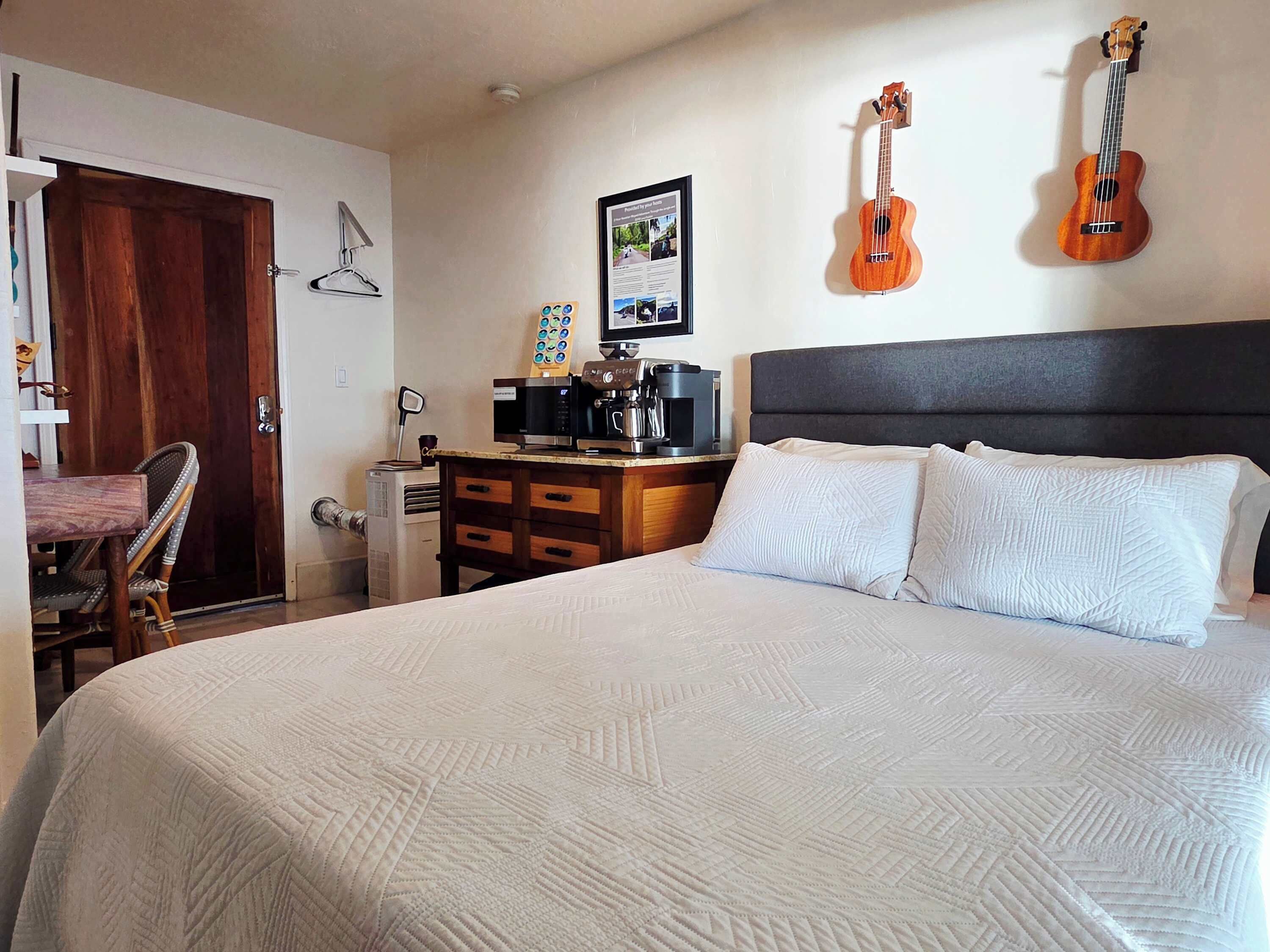 A bedroom with a bed, a dresser, a chair, a wall-mounted guitar, and a framed picture.