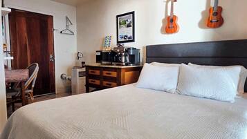 A bedroom with a bed, a dresser, a chair, a wall-mounted guitar, and a framed picture.
