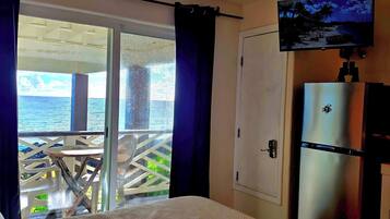 A bedroom with a bed, a television mounted on the wall, and a sliding door leading to a balcony with a view of the sea.