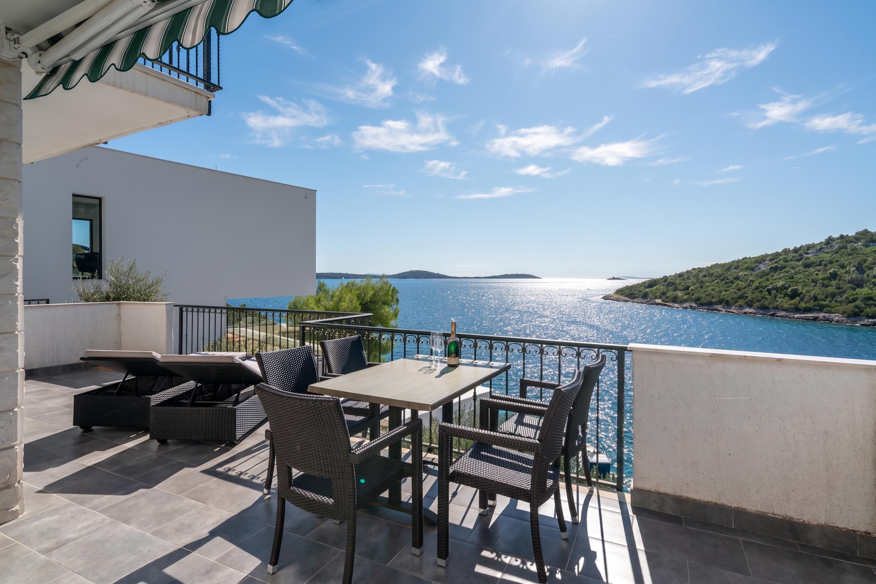 A terrace with a table and chairs, overlooking a body of water and a distant island.