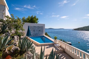 A pool with a view of the sea, surrounded by plants and a tiled wall. - Pool Villa Sine /w Panoramic Sea View (Marina)