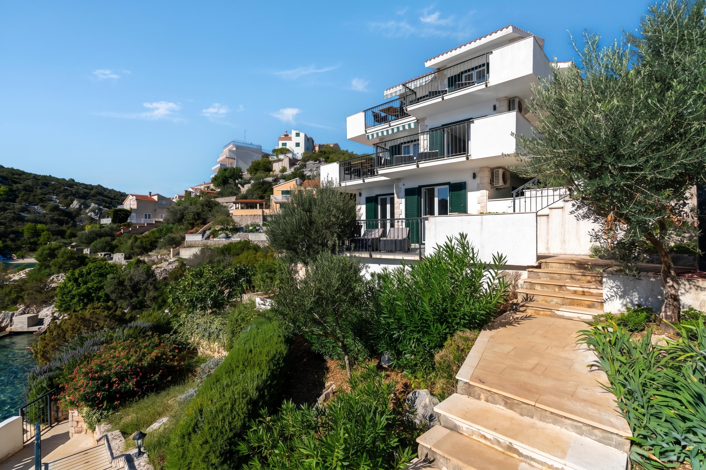 A coastal property with a modern two-story building, a stone staircase, and lush greenery.