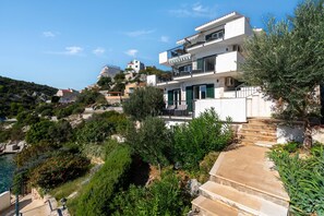 A coastal property with a modern two-story building, a stone staircase, and lush greenery. - Pool Villa Sine /w Panoramic Sea View (Marina)