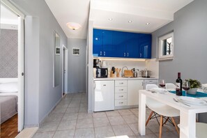 Cocina compacta con armarios blancos, comedor con mesa y sillas, y un ventanal.