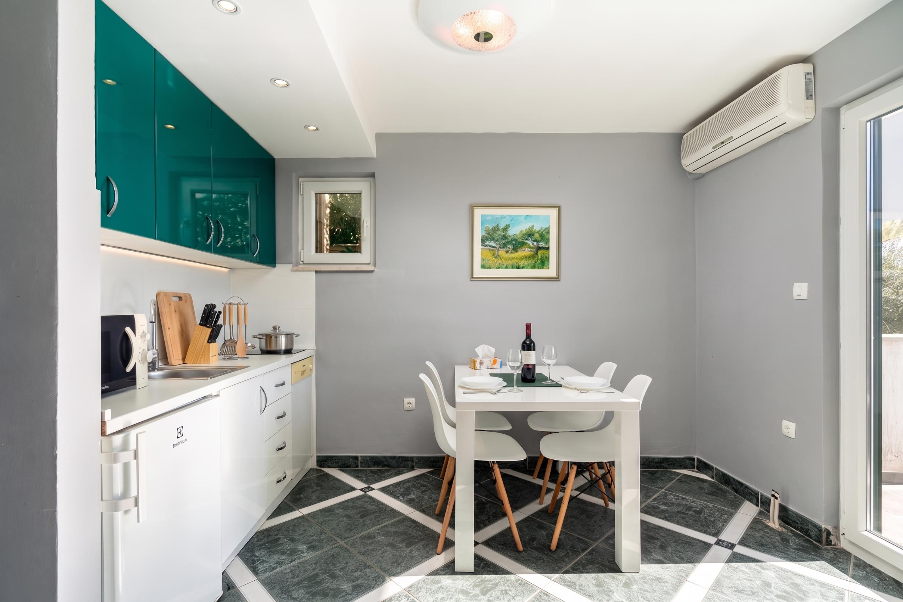 Una cocina compacta con armarios azul verdoso, una mesa de comedor con sillas y un cuadro en la pared.