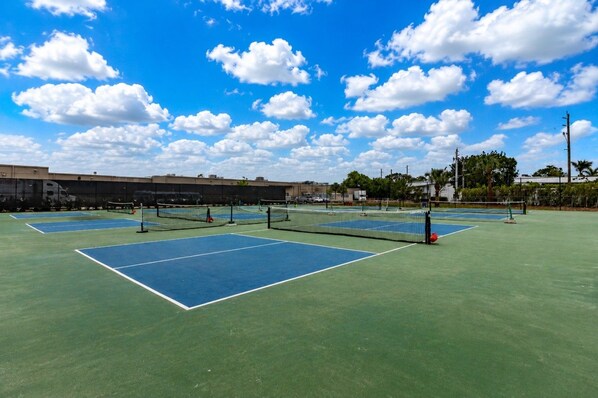 Canchas de tenis múltiples, una red y cielo despejado.