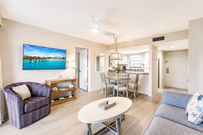 A living room with a sofa, a coffee table, a TV, and a dining area with chairs and a table. - Park Shore Resort Deluxe Condo Top FloorBLDG F#339 (Park Shore Resort)