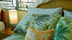 Una cama con colcha de estampado de hojas tropicales, un cojín con diseño de hojas de palma y un cabecero de madera.