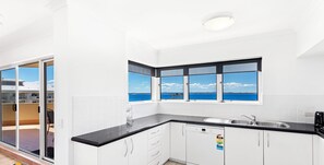 A modern kitchen with white cabinets, a black countertop, and a view of the sea through large windows. - Breakwater Apartment 402 - Looking over Shoal Bay (Shoal Bay)