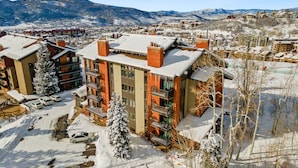 Un hôtel à plusieurs étages, dont le toit est recouvert de neige, entouré d’un parking et avec une chaîne de montagnes en arrière-plan.