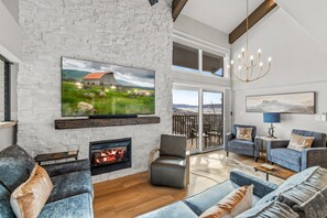 A modern living room with a fireplace, comfortable seating, a large flat-screen TV, and a scenic painting on the wall. - Bear Claw 402 Premium On Mountain Condo with Ski-In/Ski-Out Access! (Steamboat Springs)