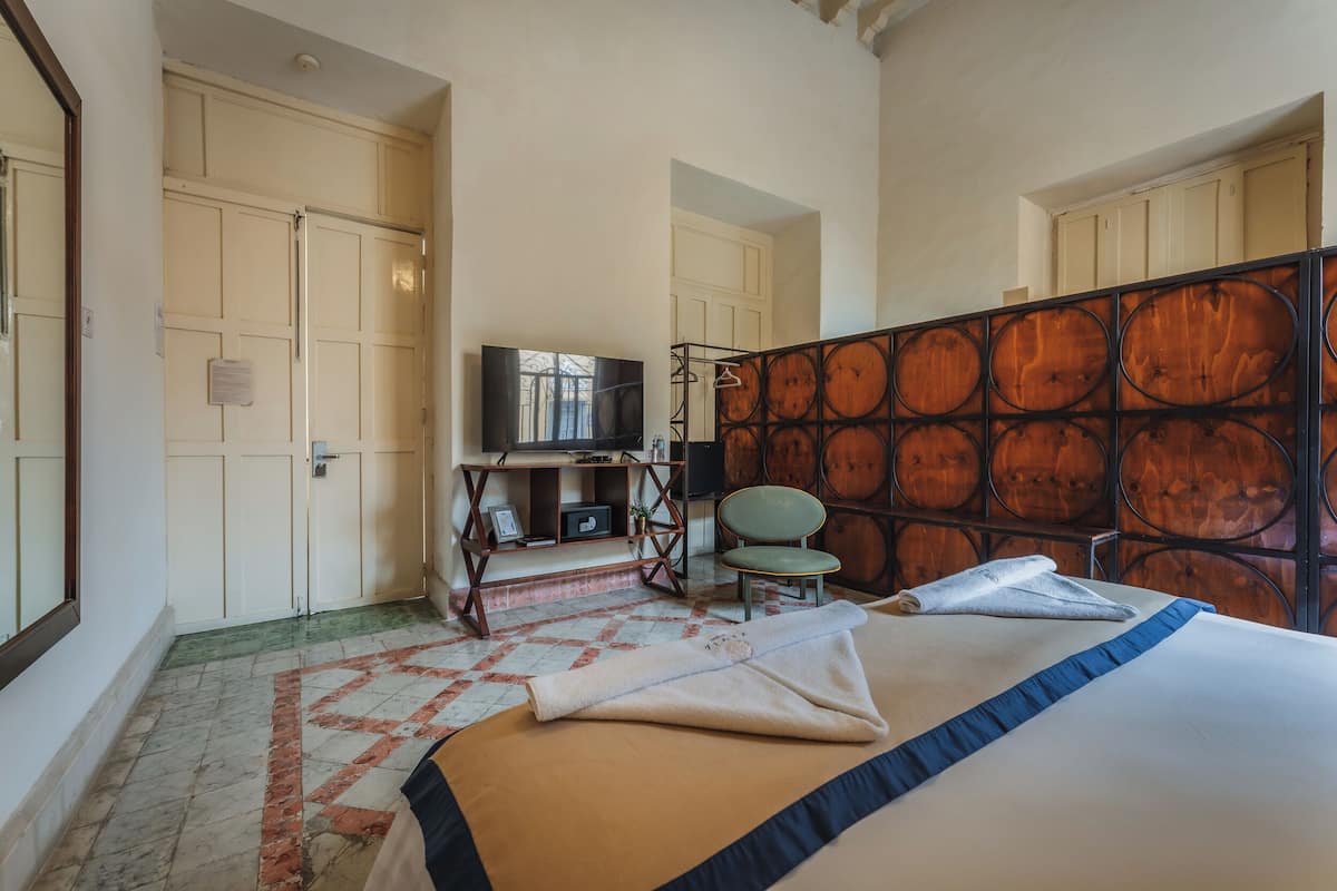 A hotel room with a bed, a TV, a chair, and a wooden partition.