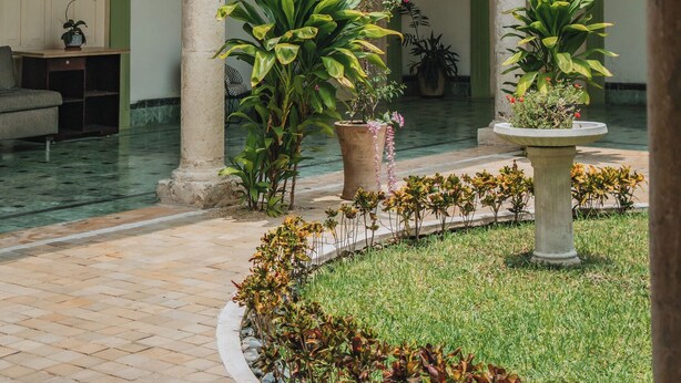 Un patio con arcos, plantas en macetas, una fuente y suelo de baldosas.