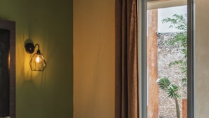 Una habitación de hotel con una cama, una mesita pequeña, una lámpara de pared y un ventanal con cortinas.