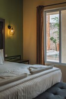 Ein Hotelzimmer mit einem Bett, einem kleinen Tisch, einer Wandlampe und einem Fenster mit Vorhängen.