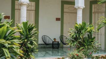 Un patio con suelo de baldosas, arcos de marco verde, plantas en macetas y una silla.