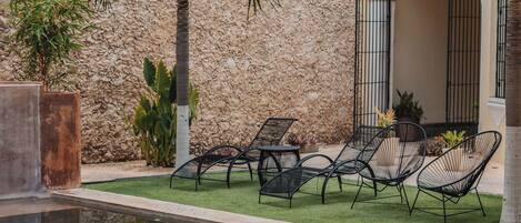 Un área de piscina con sillones de descanso, palmeras y una pared de piedra.