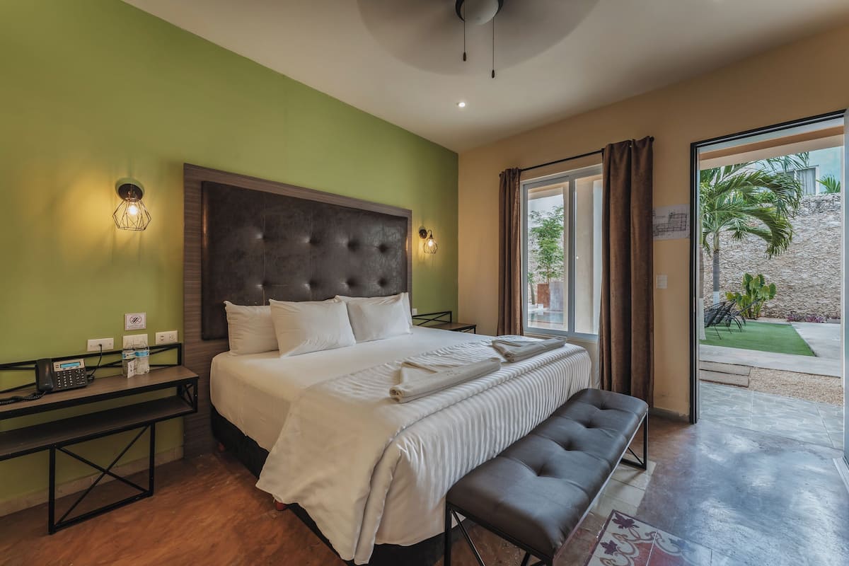 A hotel room with a large bed, a bench, a bedside table with a phone, and a view of the outdoors.